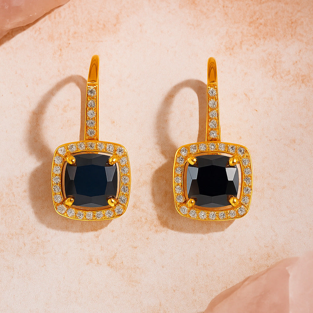 Gold earrings with black gemstones on a beige surface