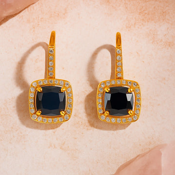 Gold earrings with black gemstones on a beige surface