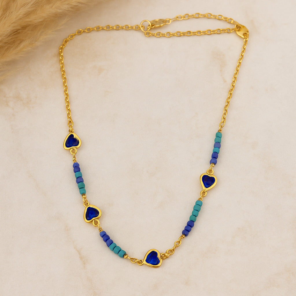 Gold necklace with heart-shaped blue pendants and blue beads on a beige background
