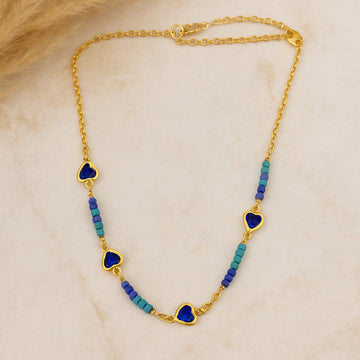 Gold necklace with heart-shaped blue pendants and blue beads on a beige background