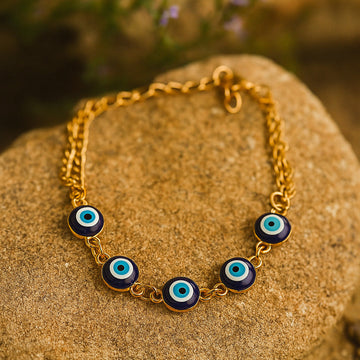 Gold bracelet with blue evil eye beads on a stone surface