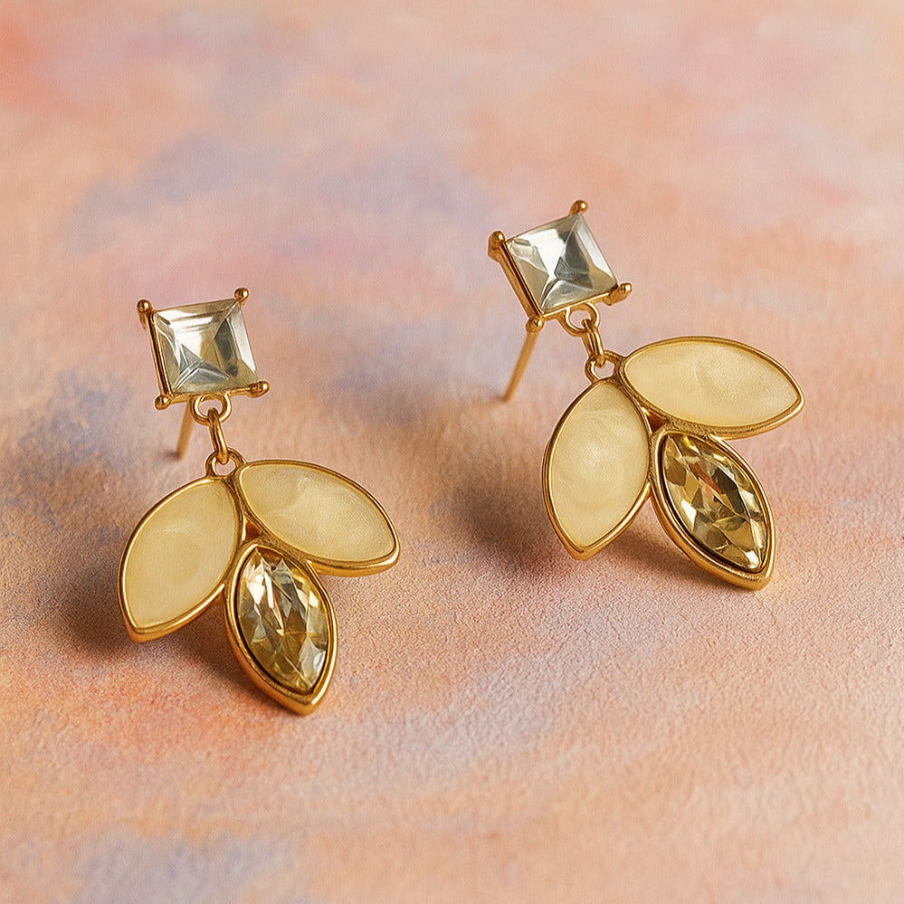 Gold earrings with leaf-shaped stones on a soft pink background