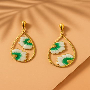 Gold earrings with green and white floral designs on a beige background