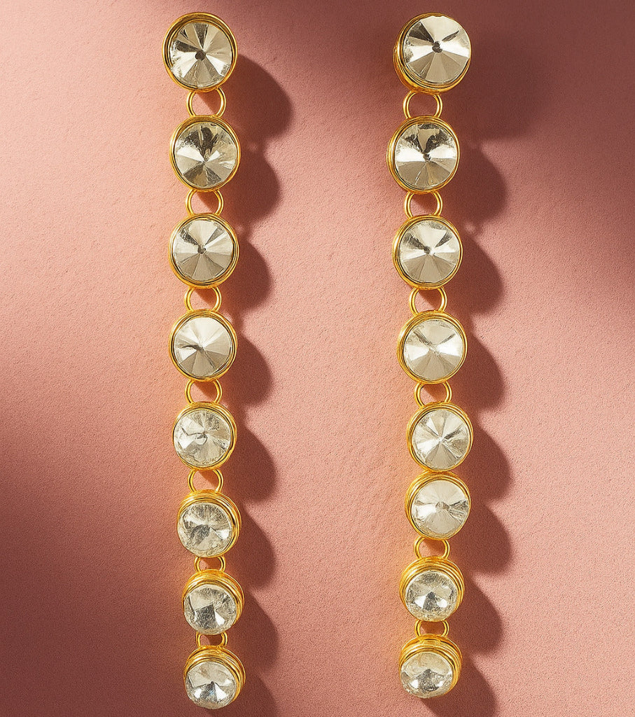 Gold and crystal drop earrings on a pink background