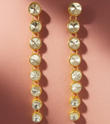 Gold and crystal drop earrings on a pink background