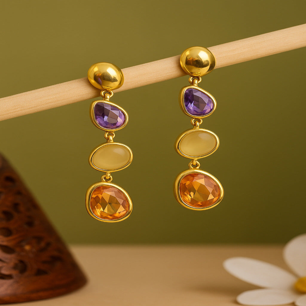 Gold earrings with multicolored gemstones on a wooden stick against a green background