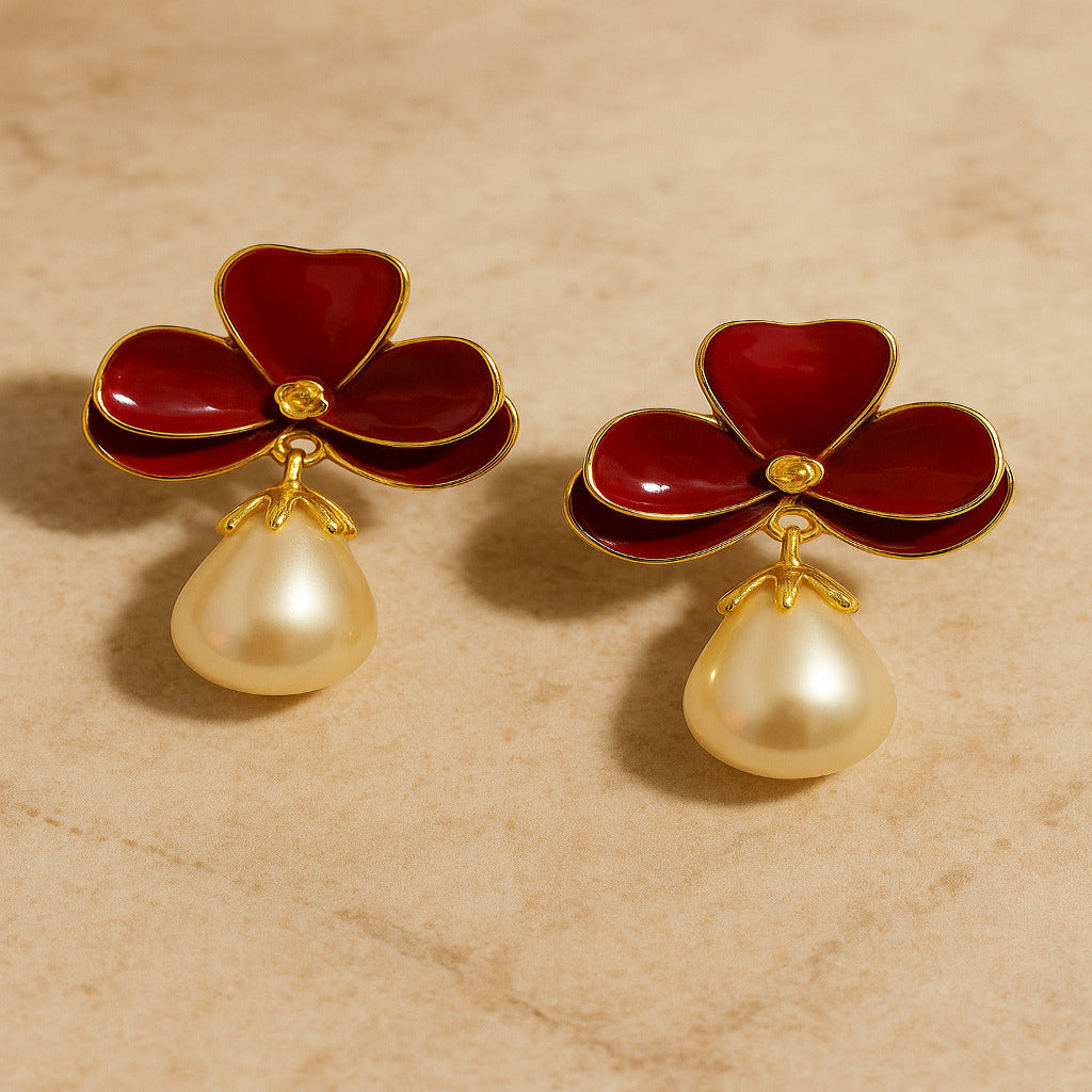 Pair of earrings with red flower-like tops and pearl drops on a beige background