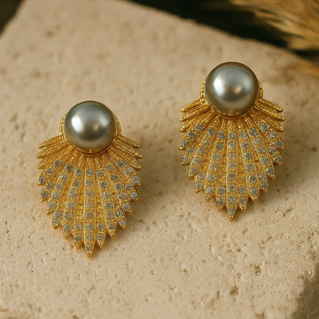 Gold earrings with pearl-like stones on a textured surface