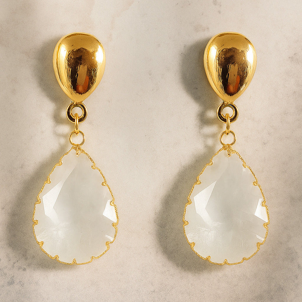 Gold earrings with teardrop-shaped white stones on a light background