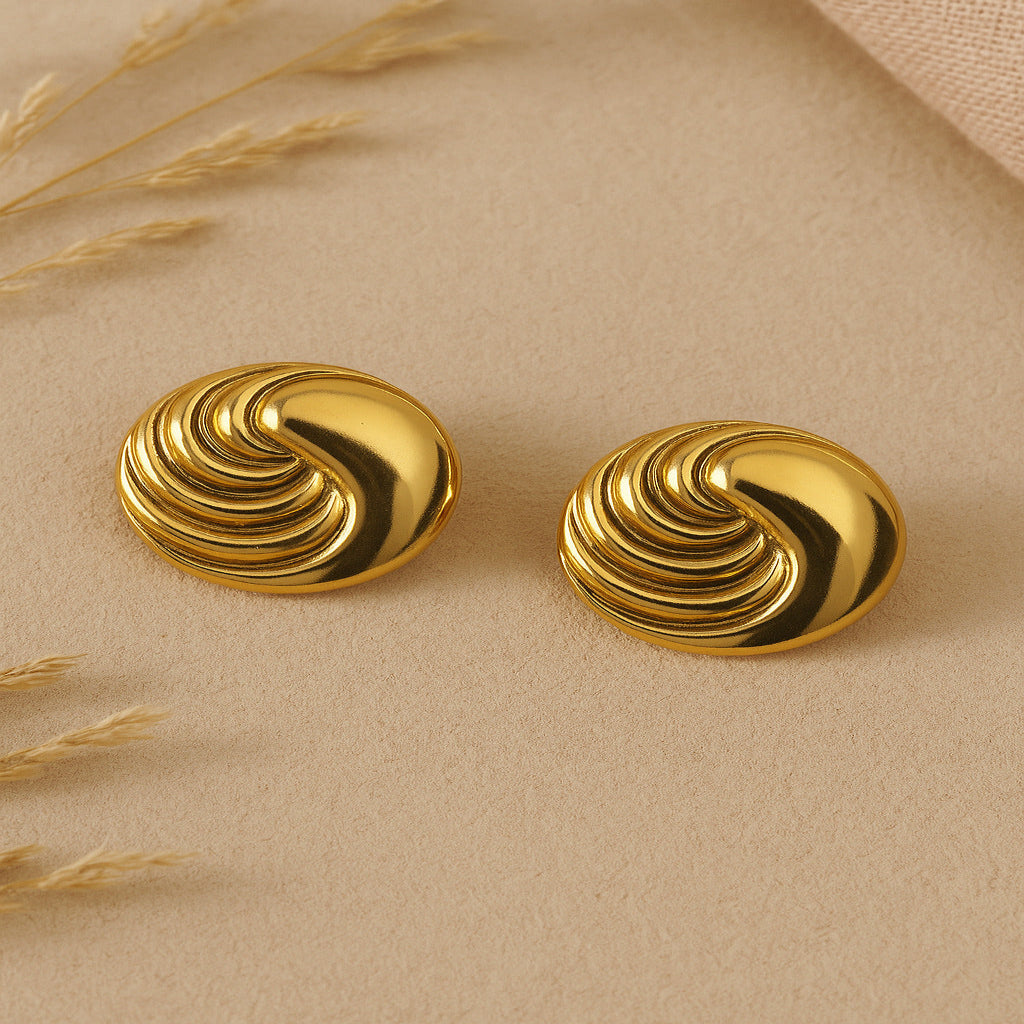Pair of gold spiral earrings on a beige surface with dried grasses.