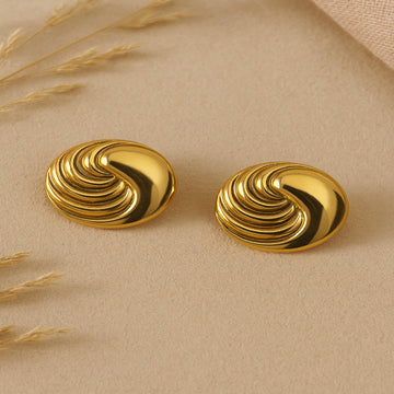 Pair of gold spiral earrings on a beige surface with dried grasses.