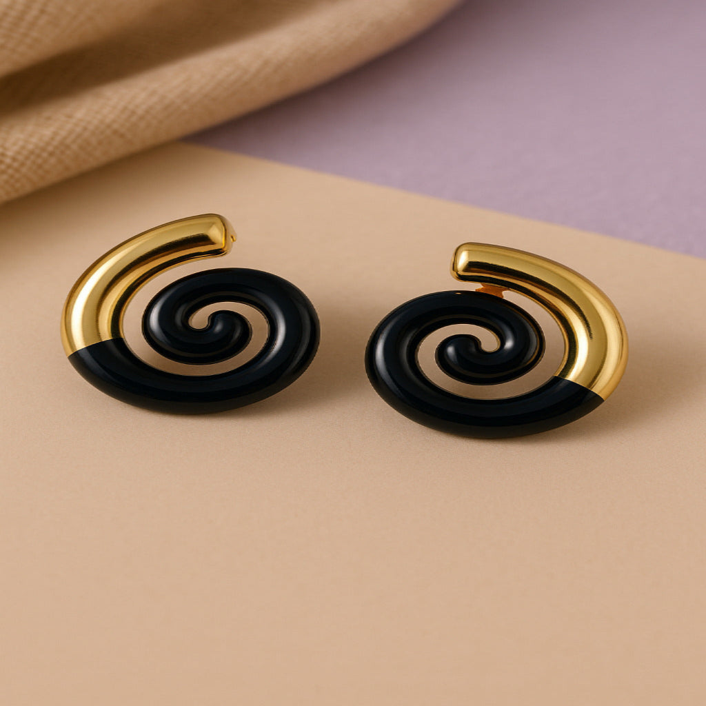 Pair of spiral earrings with gold and black design on a beige surface.