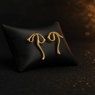 Gold earrings on a black cushion with a dark background