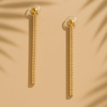 Gold earrings with clear beads on a beige background