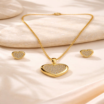 Gold heart-shaped jewelry set on a soft beige fabric background