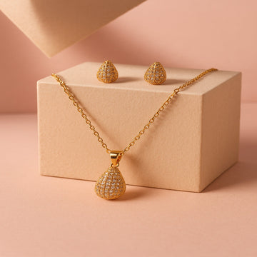 Gold necklace and earrings on a beige box with a pink background