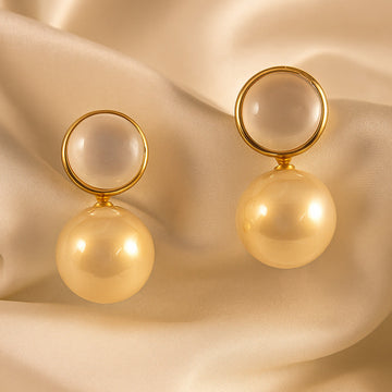 Gold earrings with spherical designs on a beige fabric background