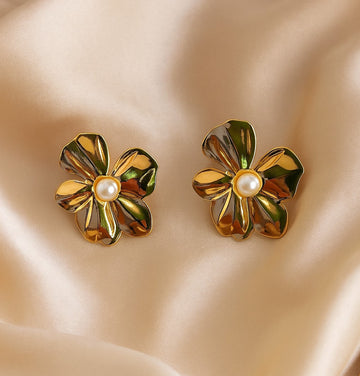 Gold flower-shaped earrings with pearl center on a beige fabric background