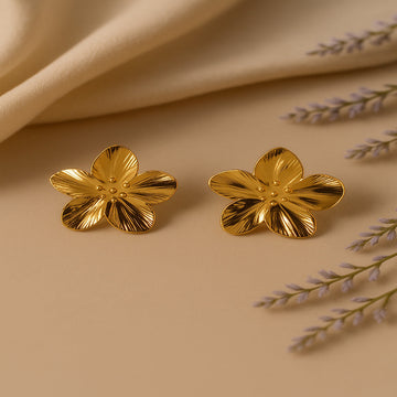 Gold flower-shaped earrings on a beige fabric background with lavender flowers.