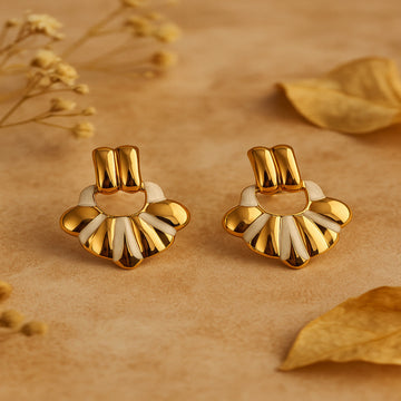Pair of gold and white earrings on a beige background with dried flowers.