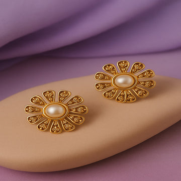 Gold earrings with pearl centers on a beige stone against a purple background