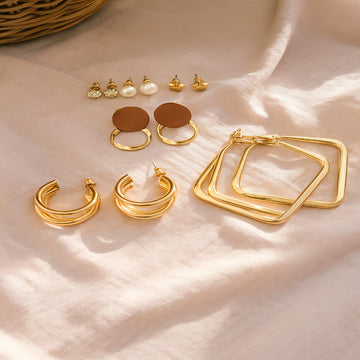 Collection of gold earrings on a soft beige fabric background
