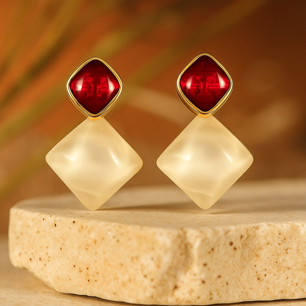 Pair of earrings with red and beige stones on a wooden platform