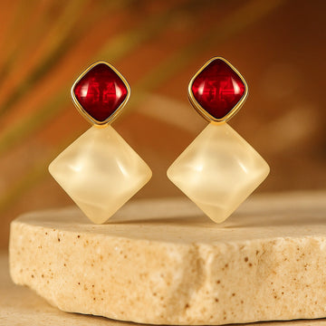 Pair of earrings with red and beige stones on a wooden platform