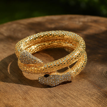 Gold snake-shaped bracelet with gemstones on a wooden surface