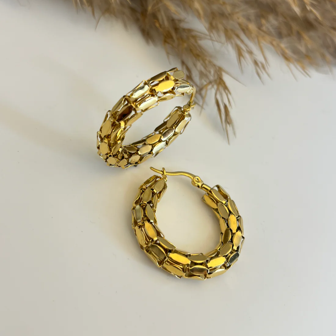 Gold hoop earrings on a light background with dried grasses.