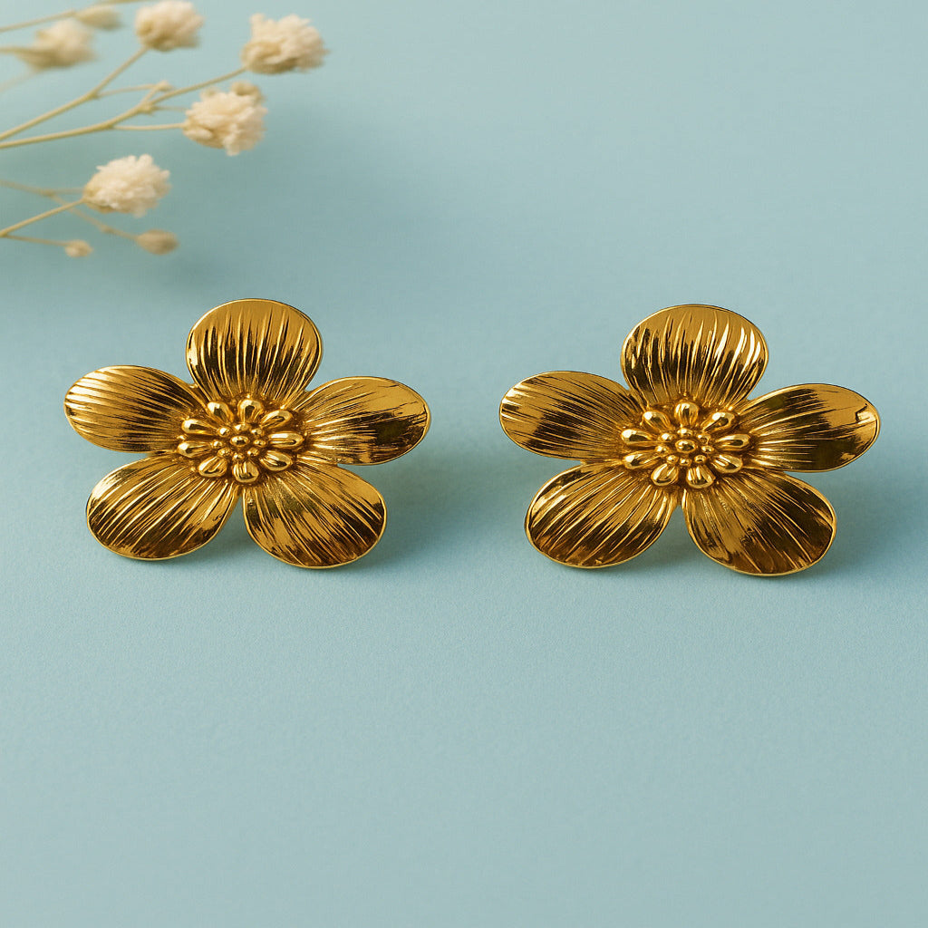 Pair of gold flower-shaped earrings on a light blue background