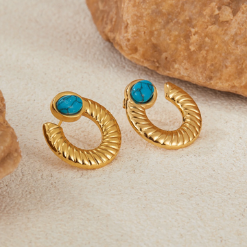 Gold hoop earrings with turquoise stones on a textured beige surface