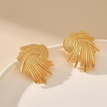 Gold feather-shaped earrings on a beige background