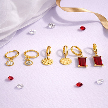 Set of gold and red earrings on a light purple fabric background
