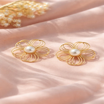 Gold flower-shaped earrings with pearls on a soft pink fabric background