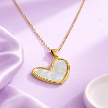 Heart-shaped pendant necklace with gold frame and light-colored stone on a pink background