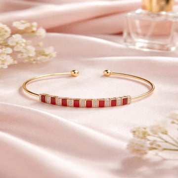 Gold bracelet with red accents on a pink fabric background