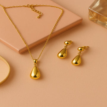 Gold necklace and earrings on a beige surface