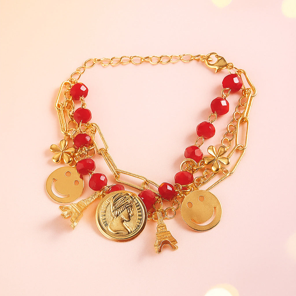 Gold bracelet with red beads and various charms on a pink background