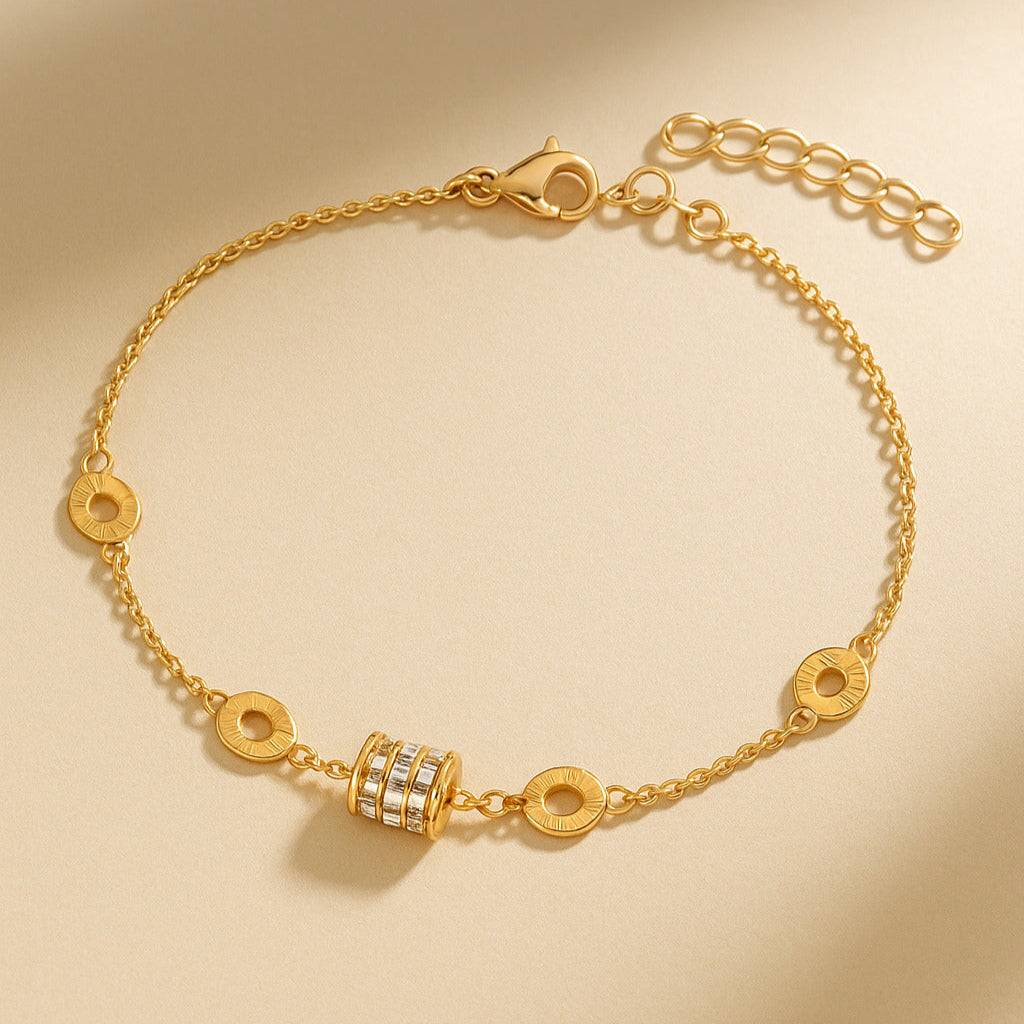 Gold bracelet with a cylindrical charm on a beige background