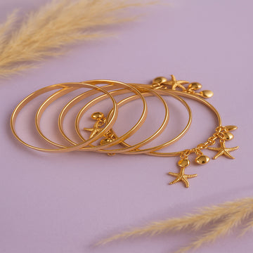 Set of gold bangles with starfish charms on a light purple background