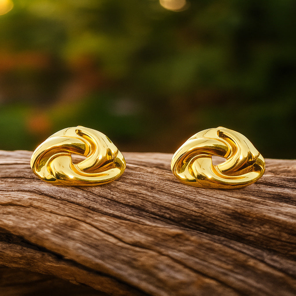 Pair of gold earrings on a wooden surface with a blurred natural background