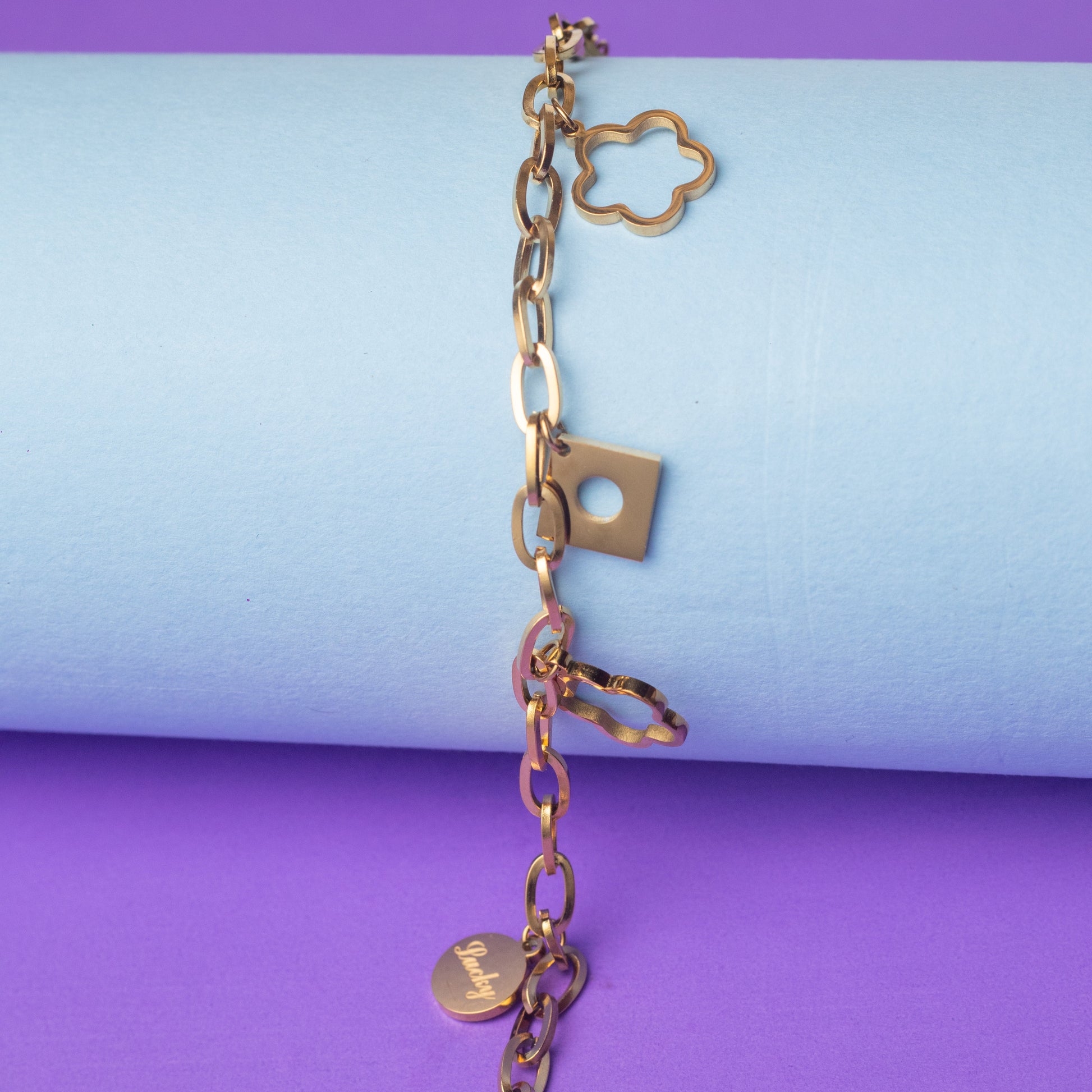 Gold chain bracelet with various links on a purple and blue background
