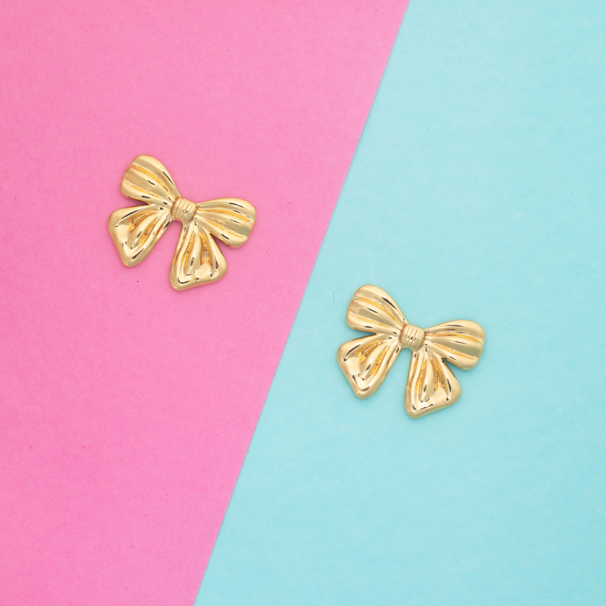 Gold bow-shaped earrings on a pink and blue background