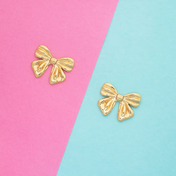 Gold bow-shaped earrings on a pink and blue background