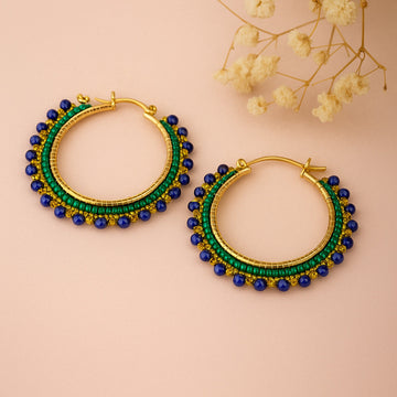 Gold hoop earrings with green and blue beads on a beige background