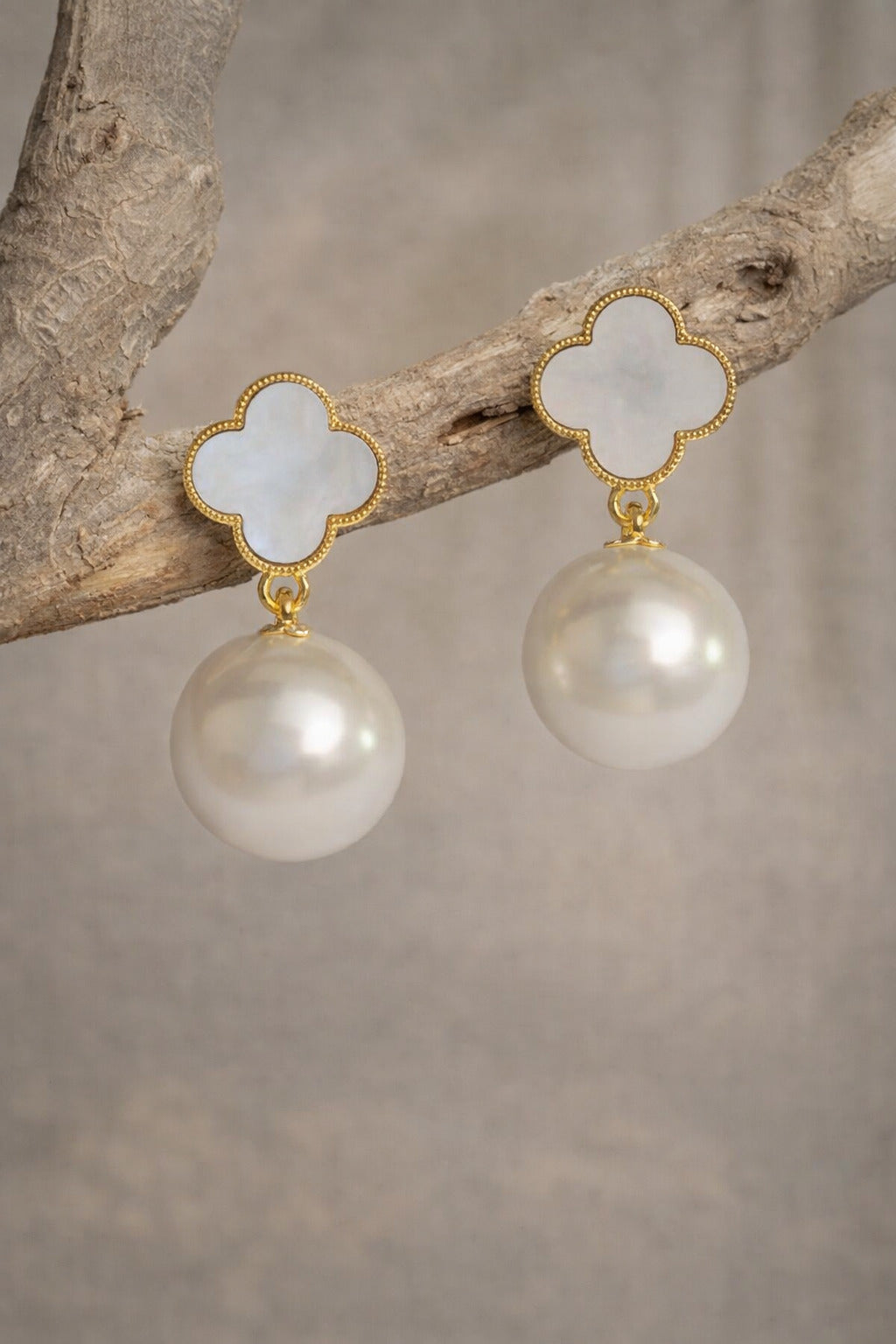 Pearl earrings with gold accents on a branch against a neutral background