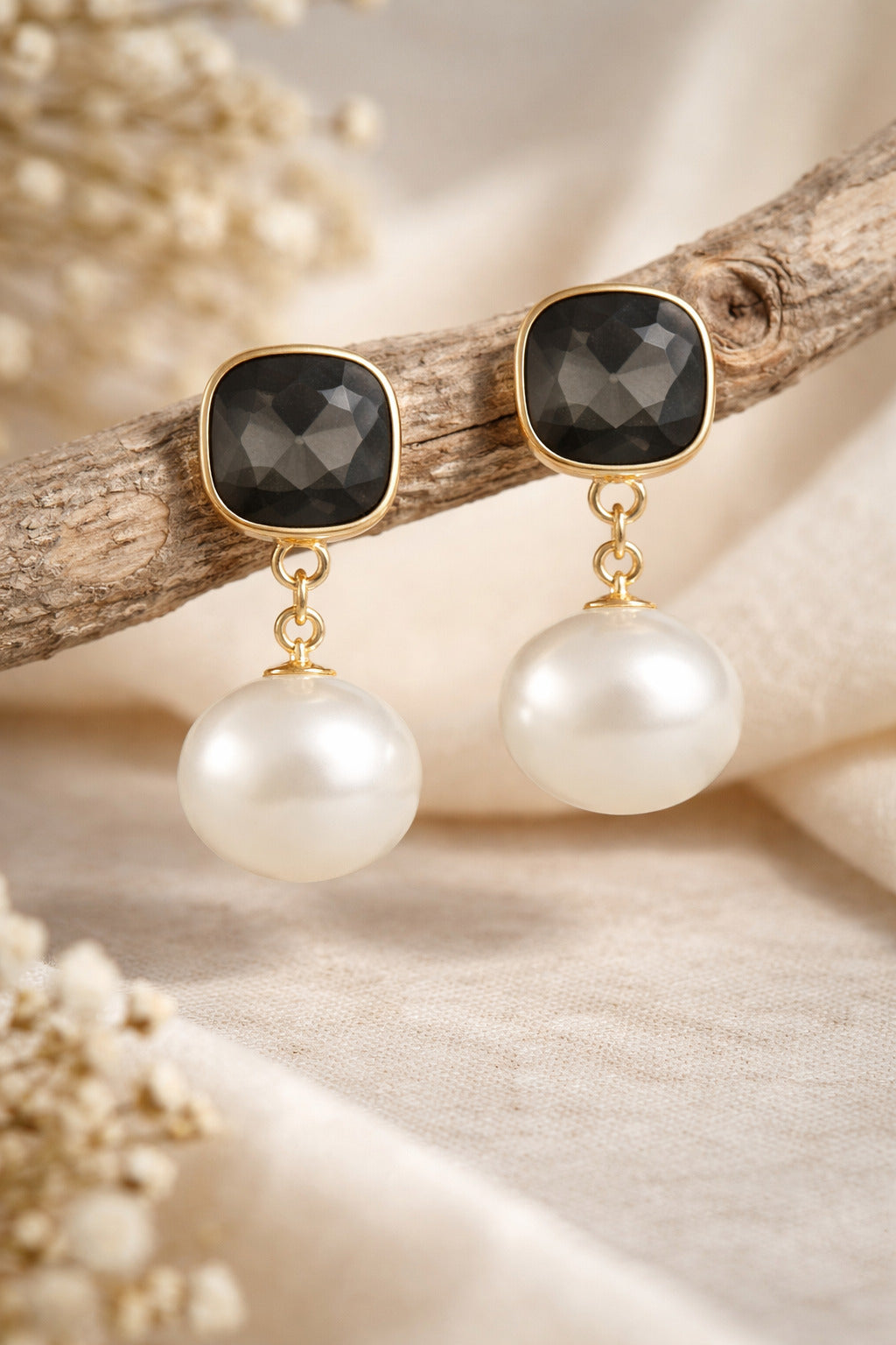 Pair of earrings with gold accents, black gemstones, and white pearls on a natural background.