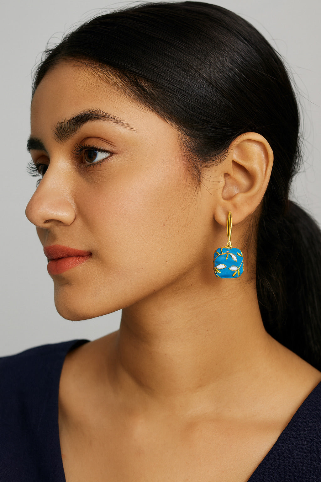 Woman wearing a blue earring with a gold hook on a plain background