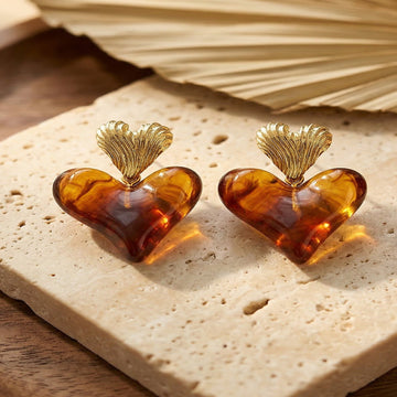 Heart-shaped amber earrings with gold tops on a beige stone surface.